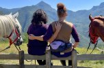 Two trail riders sitting together on a bench with their horses, enjoying a mountain view during a horseback riding holiday