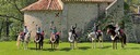 Trail riders standing on a meadow in front of a church in a Spanish mountain village, waving