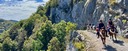 Group of trail riders on a wide gravel road beside a rock wall, looking down into a mountain gorge
