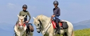 Two female trail riders on a mountain summit in the Pyrenees, riding white Andalusian horses
